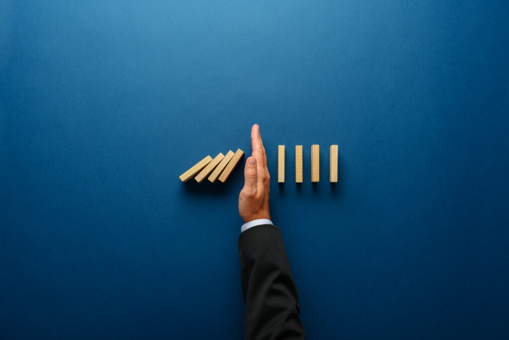 Business hand stopping falling dominoes, symbolizing risk management